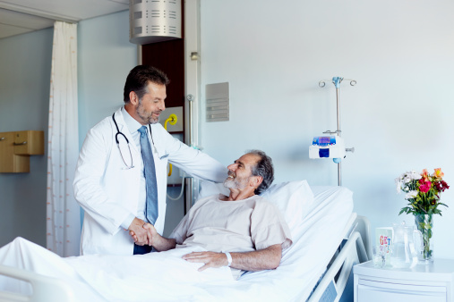 Male doctor greeting patient lying in bed at hospital ward