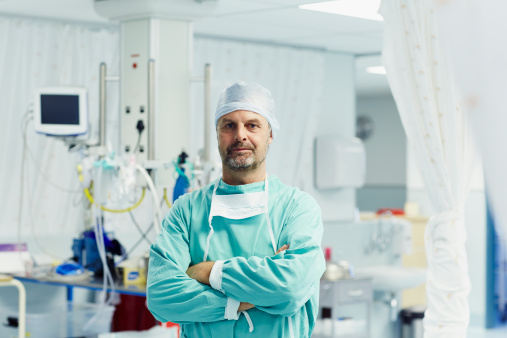 Portrait of confident male surgeon standing arms crossed in operating room at hospital