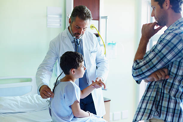 Father looking at doctor examining son in hospital Father looking at doctor examining son with stethoscope in hospital ward sick child hospital bed stock pictures, royalty-free photos & images