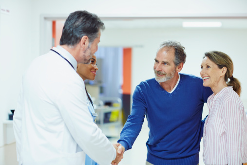 Male doctor greeting happy mature couple in hospital