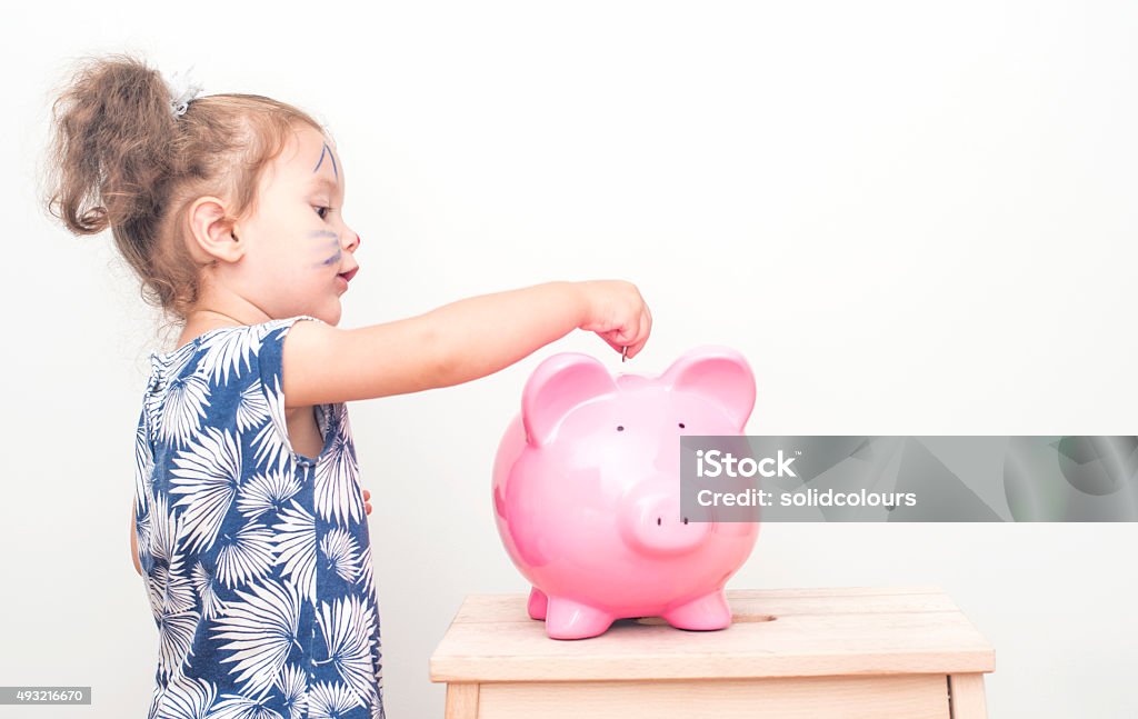 Little Girl Placing Coin In Piggy Bank. Two years girl placing a coin in a piggy bank. Child Stock Photo