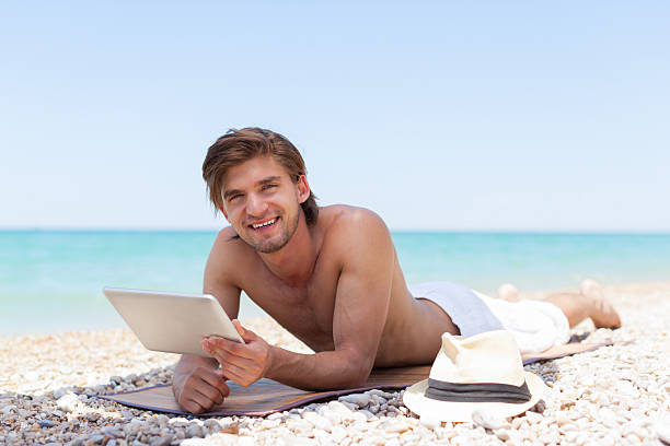 homme utiliser une tablette ordinateur allongé sur la plage, smile - reading beach e reader men photos et images de collection