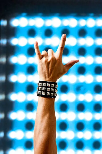 Man in wristband making rock symbol. Concert lighting.