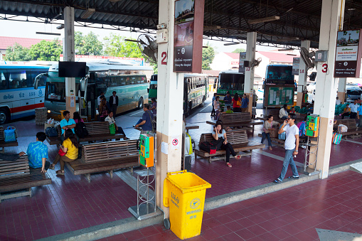 Lampang, Thailand - March 1, 2013: Capture of waiting thai people and buses in Lampang bus station in forenoon. People are sitting in benches. A man is selling lottery fortunes.