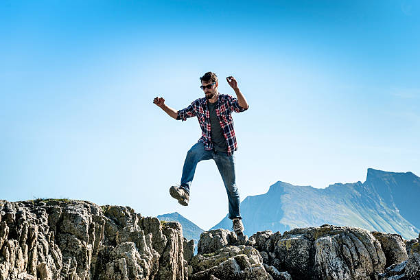 istock Young man with a beard jumps from rock to rock. 493238830
