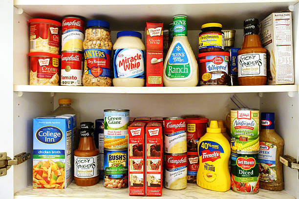 Kitchen pantry shelves filled with groceries West Palm Beach, USA - October 9, 2015: Image of two kitchen pantry shelves filled with groceries. Included among the groceries are canned soups, tomatoes, beans and corn, salad dressings, barbecue sauce, peanuts, mustard, cake mixes, chicken broth, and a variety of other cooking and baking ingredients. Many popular brand names are represented, such as Campbells, Green Giant, Del Monte, Bush's, Miracle Whip, Betty Crocker, Libbys, Duncan Hines and Kraft convenience food photos stock pictures, royalty-free photos & images