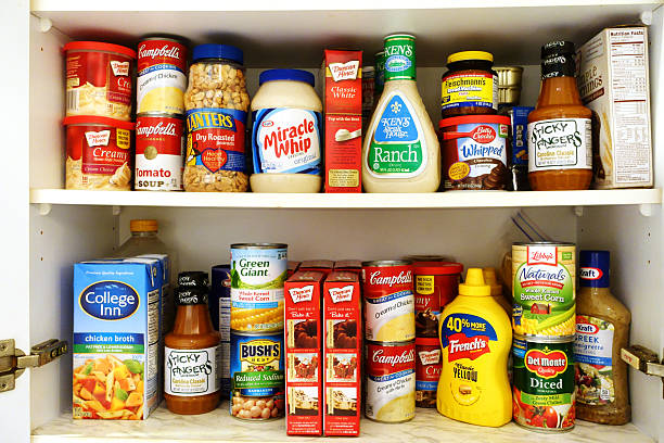 Kitchen pantry shelves filled with groceries West Palm Beach, USA - October 9, 2015: Image of two kitchen pantry shelves filled with groceries. Included among the groceries are canned soups, tomatoes, beans and corn, salad dressings, barbecue sauce, peanuts, mustard, cake mixes, chicken broth, and a variety of other cooking and baking ingredients. Many popular brand names are represented, such as Campbells, Green Giant, Del Monte, Bush's, Miracle Whip, Betty Crocker, Libbys, Duncan Hines and Kraft Ready To Eat stock pictures, royalty-free photos & images