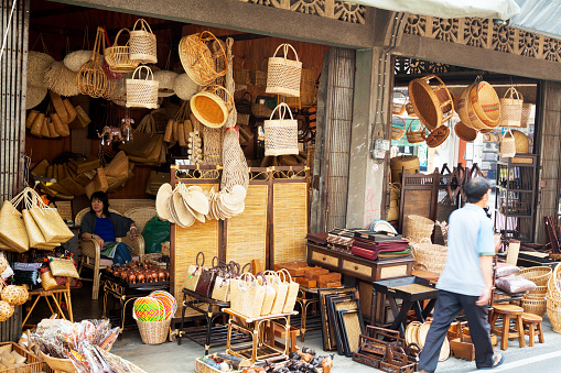 Chiang Mai, Thailand - February 26, 2013: Capture of an shop selling bamboo home decor and utensils in Chiang Mai. Vendor and woman is sitting inside of shop. A thai man is walking in street.