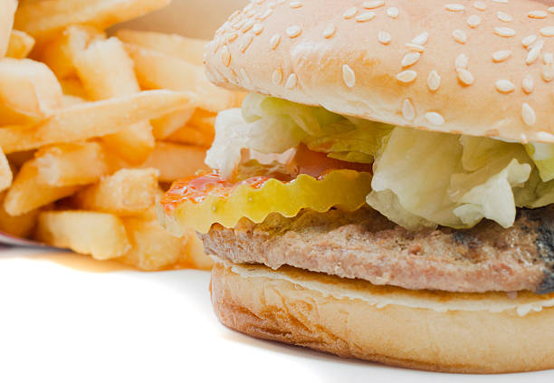 A burger with pickles, lettuce, tomatoes, mayonnaise, ketchup and more in close focus with a stack of fries in soft focus in the background.