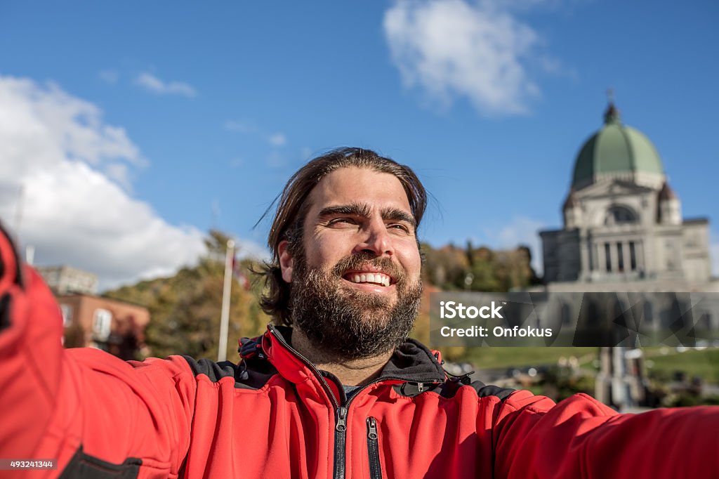 Man Doing Selfie in Front of Saint Joseph's Oratory, Montreal DSLR picture of a man tourist doing a selfie in front of the St Joseph Oratory in Autumn, Montreal, Quebec. It is a beautiful fall day. The man is happy and smiling. The Saint Joseph's Oratory is a Roman Catholic minor basilica and national shrine on Westmount Summit in Montreal, Quebec. It is Canada's largest church. 2015 Stock Photo