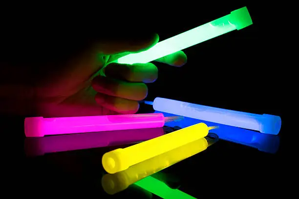 A hand holding green glow stick,with other color glow sticks on a dark background