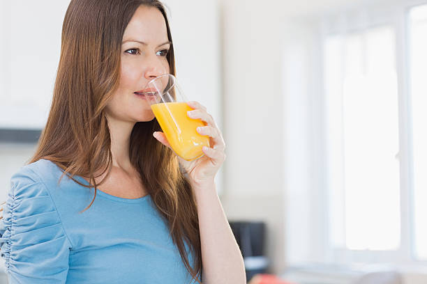 istock Side view of a woman drinking orange juice in kitchen 493246575