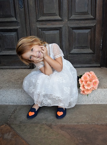 An asorable little girl sits on the church steps with her head I  hands