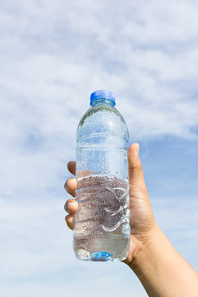 istock hand holding water bottle on cloud and sky 493248580