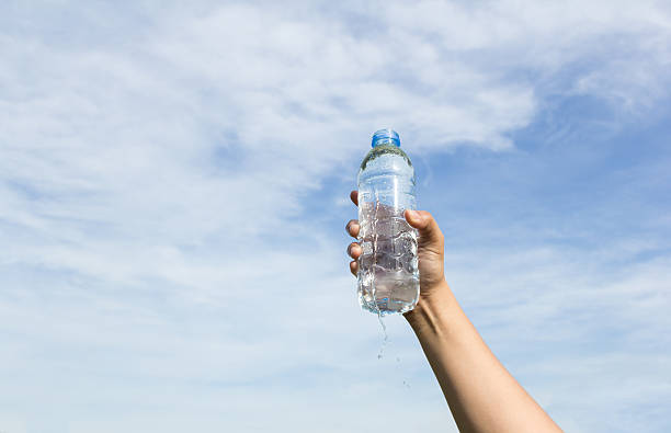 istock hand holding water bottle on cloud and sky 493248608