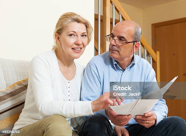 Mature Couple With Documents At Home Stock Photo - Download Image Now - 60-69 Years, Couple - Relationship, Document