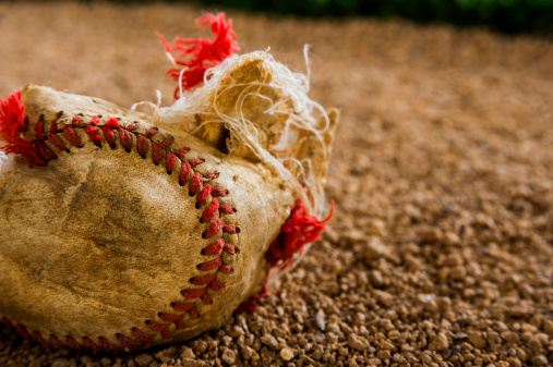 A Close-up of an Old Shredded Baseball in the dirt next to grass