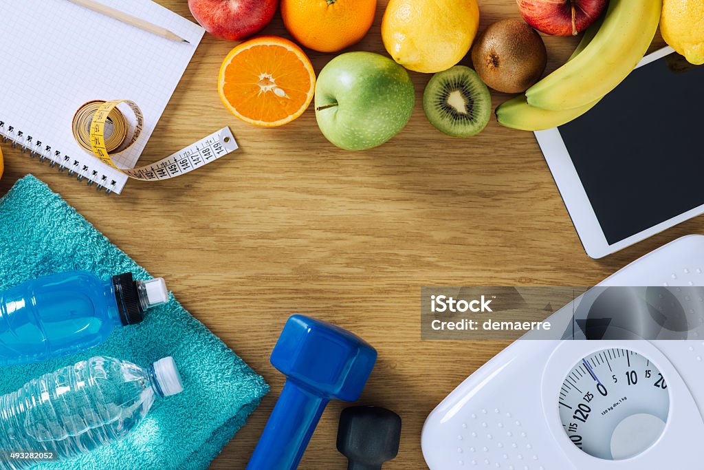 Fitness and weight loss Fitness and weight loss concept, dumbbells, white scale, towels, fruit, tape measure and digital tablet on a wooden table, top view Aspirations Stock Photo