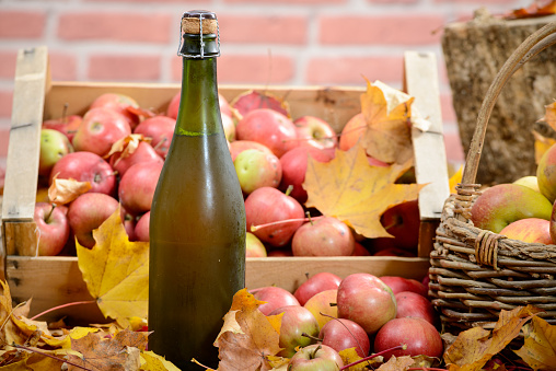 Cider bottle surrounded by red apples on autumn leaves