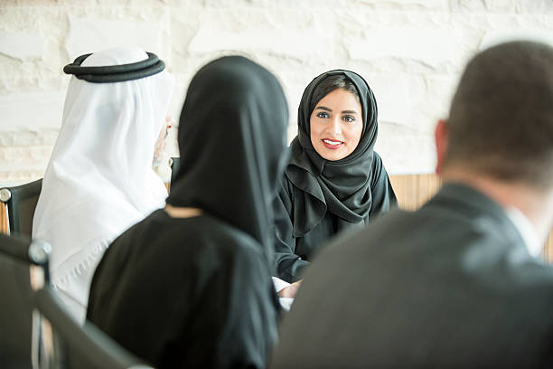 Young Middle Eastern businesswoman in business meeting Attractive young ethnic Arab businesswoman in traditional clothing smiling in meeting with male and female colleagues. Young Arabic woman in hijab and abaya in small group of business people. arabian peninsula photos stock pictures, royalty-free photos & images