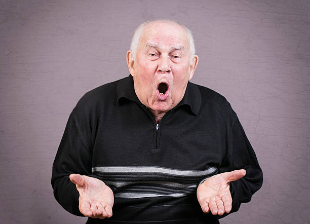 istock Very emotional old man gesticulates hands on a gray background. 493315000