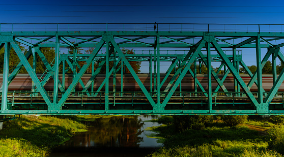 Train passing on the metal railway bridge through the small river