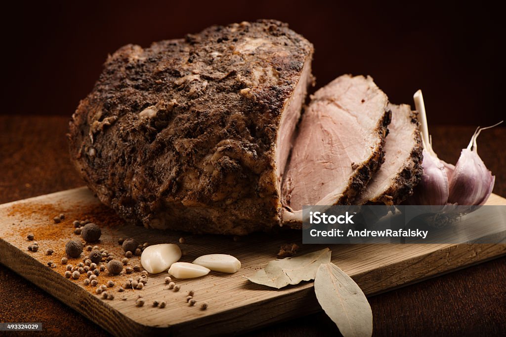 Sliced cold boiled pork with garlic, bay leaves and spices Sliced cold baked pork with garlic, black pepper, bay leaves, curry pepper and spices on a wooden cutting board laying on kitchen table, shot on dark background Bay Leaf Stock Photo