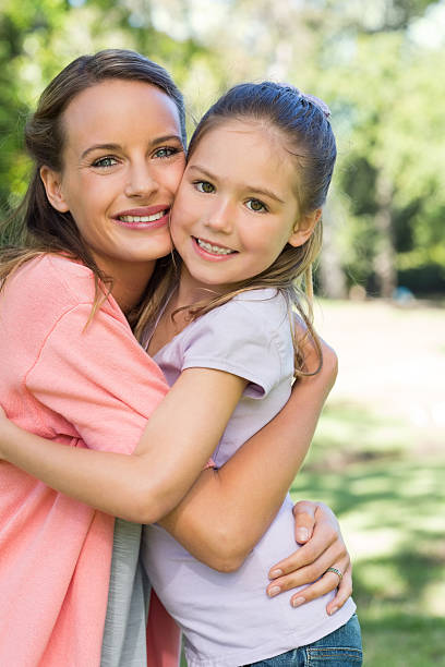 Daughter and mother hugging in park Side view portrait of happy daughter and mother hugging each other in park cheek to cheek stock pictures, royalty-free photos & images