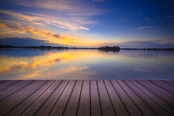 Brand new wooden recreational swimming deck on the lakeside during spectacular sunset over water.