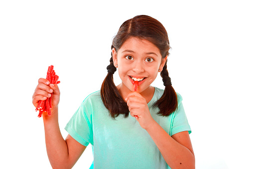 happy cute female child licking and eating red licorice candy in kid love sweet and sugar concept isolated on white background