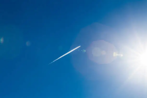 Jet with jet stream and lens flare (backlit directly in the sun) in clear blue sky at the Netherlands North Sea region.