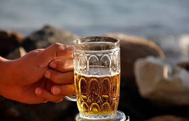 Photo of Man holding a mug of beer at a rocky beach