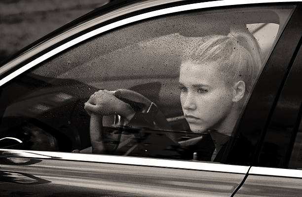 sad woman at driver seat in her car behind window full of rain drops