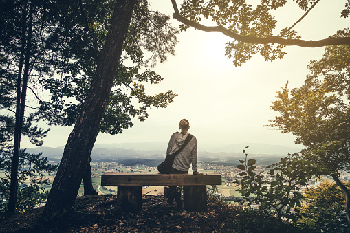 Young woman sitting on bench on top of the hill looking down on her home town.