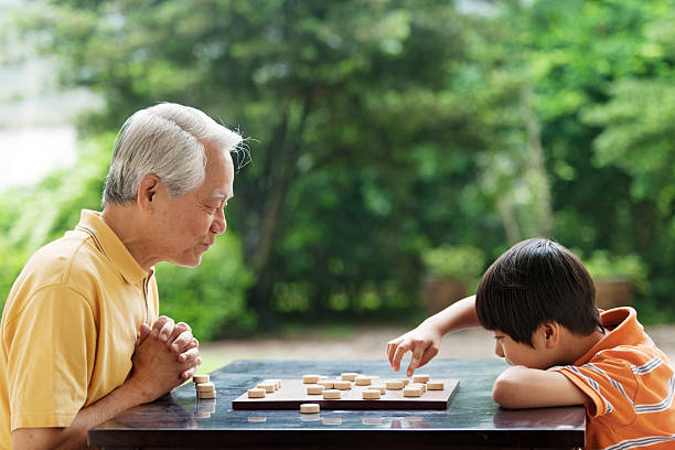 nonno e nipote a giocare a scacchi xiangqi (cinese) - concentration chess playing playful foto e immagini stock