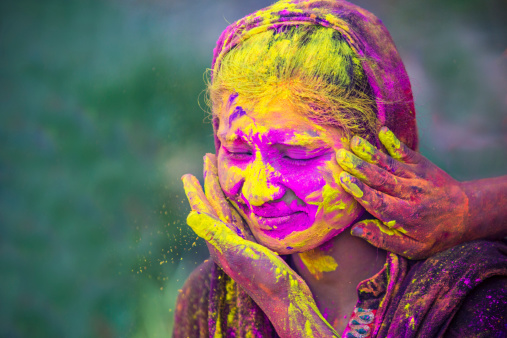Woman getting her face full of Holi colours by her friends.
