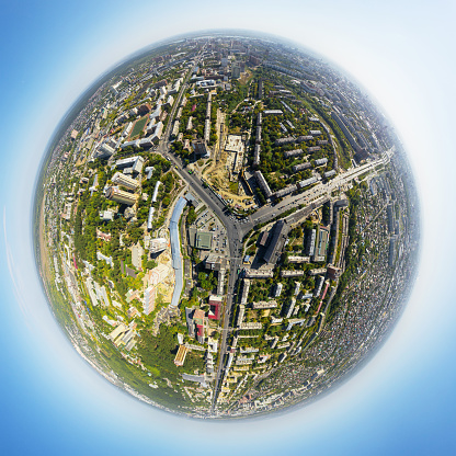 Aerial city view with crossroads and roads, houses, buildings, parks and parking lots, bridges. Copter shot. Little planet sphere mode.