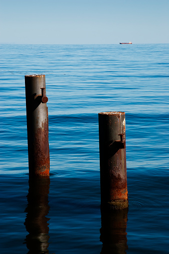Two rusty steel poles at the end of Ahlbeck pier on baltic sea island Usedom and a tanker on the distant horizon. Usedom, Germany. September 2015