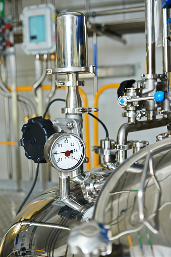 Closeup of  pharmaceutical factory equipment manometer, pipes, faucet valves, mixing tank on production line in pharmacy industry manufacture factory 