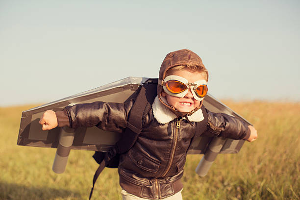 Young Boy wearing Jetpack is Taking Off A young boy wearing a bomber jacket and goggles is ready to fly his homemade jetpack. He is standing in the tall grass with arms raised on a hill in England ready for adventure. piloting stock pictures, royalty-free photos & images