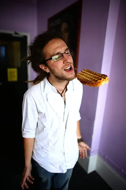 Young man opening his mouth to take a bite from a floating sandwich.