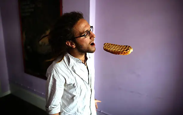 Young man opening his mouth to take a bite from a floating sandwich.