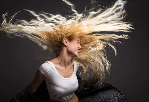 Beautiful young blond woman dancing on black background.