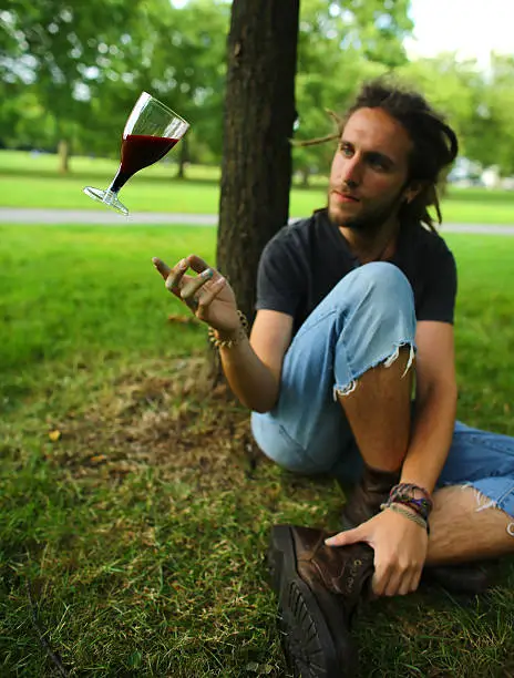 Man with dreadlocks making a wine glass float in mid-air in a park.