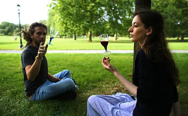 Young man and woman sitting together in a park as two wine glasses float in front of them.