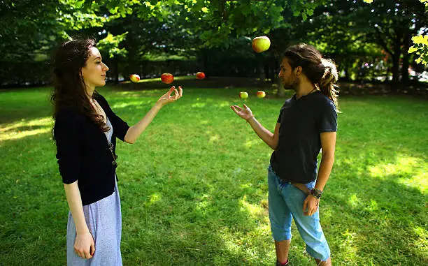 Man and woman in park under a tree as the man makes an apple float using telekinesis.