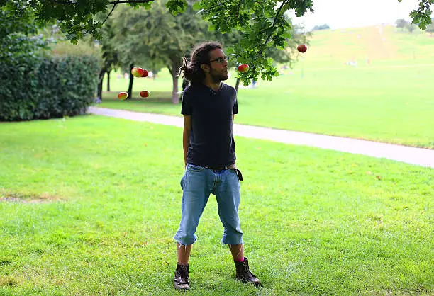 Man with dreadlocks making apples float in mid-air in a park.