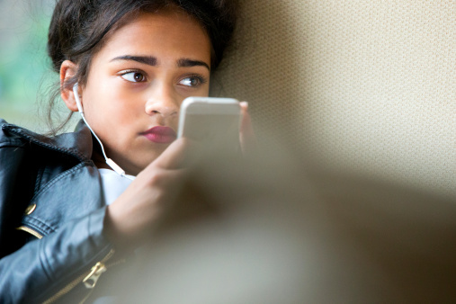 Young girl early teens playing on her phone and listening to music wearing headphones