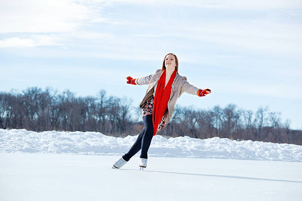 Teenage Girl Figure Skating on Winter Lake Ice Rink, Minneapolis A cute teenage girl leisurely figure skating outdoors on a pond ice rink on a cold winter day. She wears a gray jacket, skirt, tights, red neck scarf and mittens for warmth as she extends arms and glides on one foot in a Lake Harriet urban park, Minneapolis, Minnesota. ice skating photos stock pictures, royalty-free photos & images