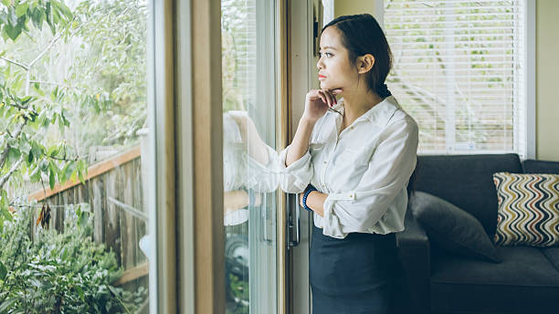 istock standing asian woman looking out   window at home 493475444